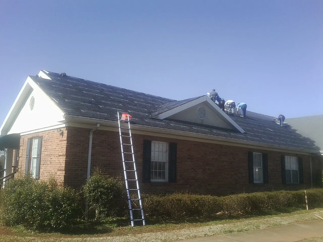 Crew tearing shingles off a brick ranch roof with a ladder set — Metal Roof Repair work by our crew in Murphy