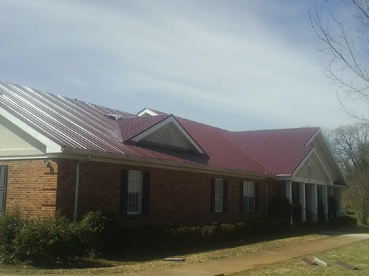Red metal roof with gabled entries on a long brick building, from a Hail Damage Roof Repair job in Murphy