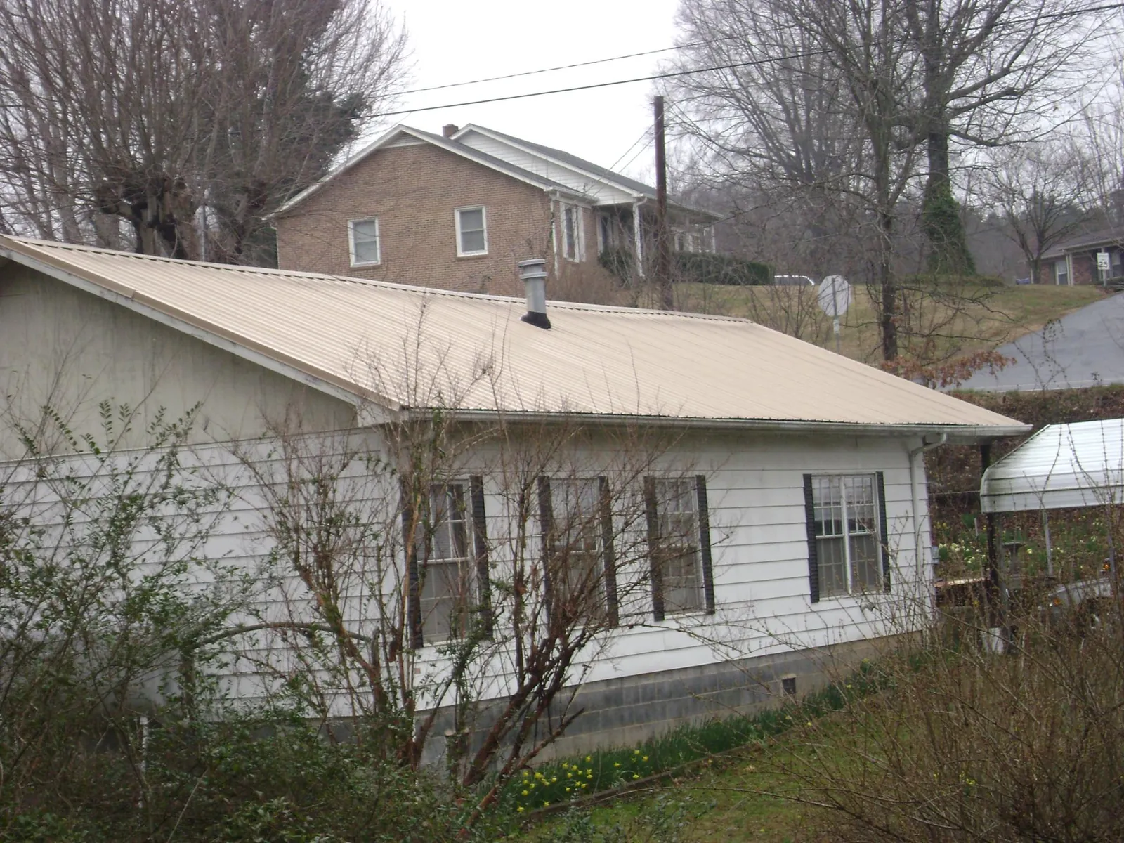 Tan metal roof on a white sided house set into a hillside — Commercial Roofing by Roofing Brothers in Murphy